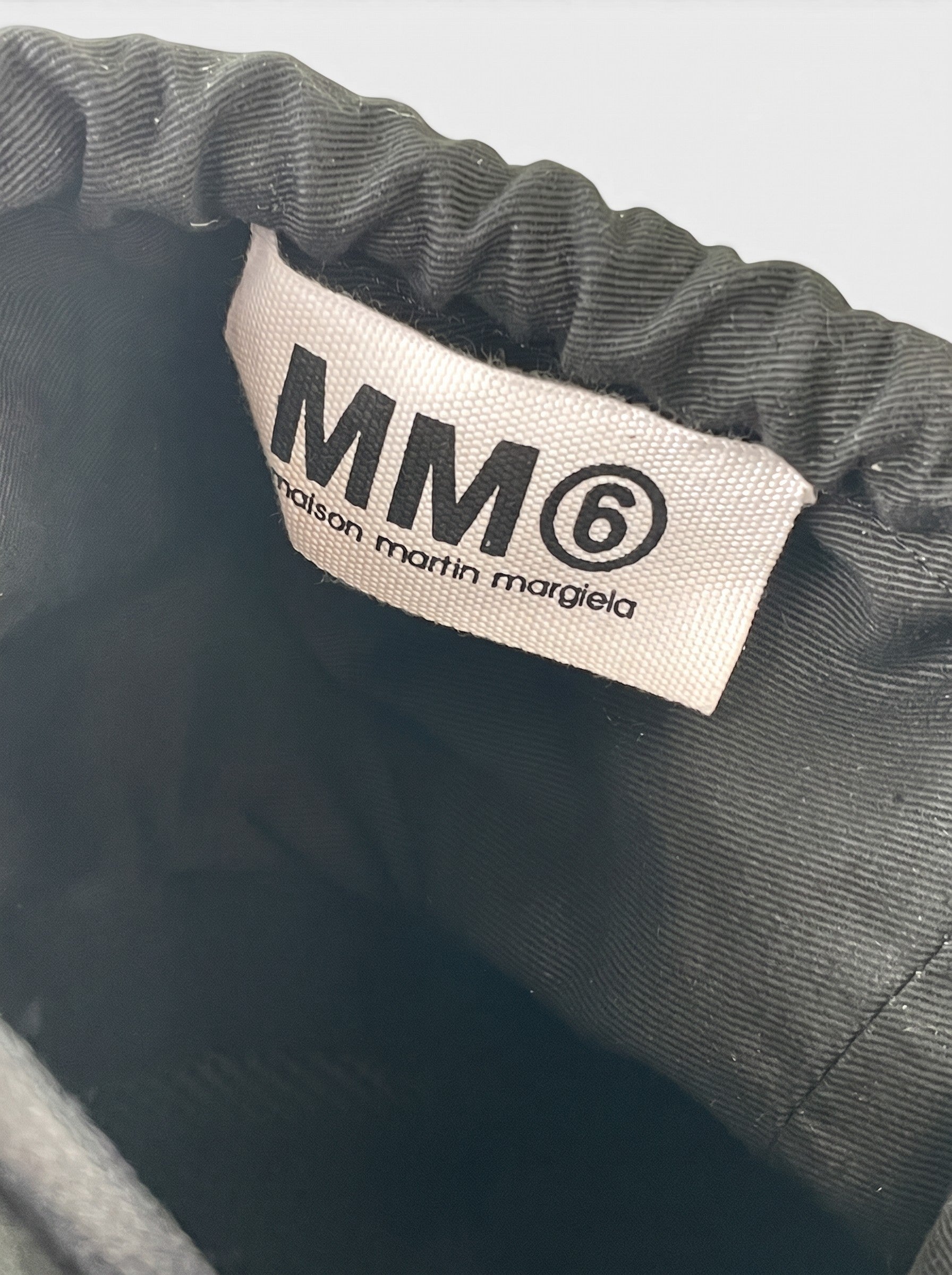Innenansicht der opening act. Maison Margiela Helm-Umhängetasche mit schwarzem Stoffbeutel und MM6 Markenetikett